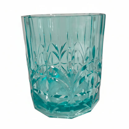 Turquoise glass tumbler with floral etching on a light pink background